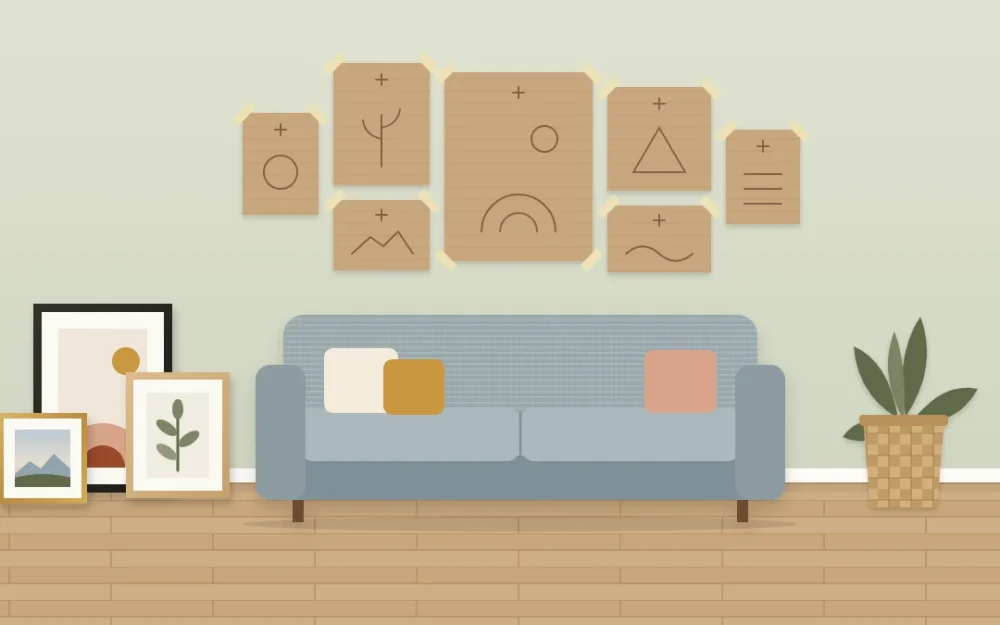 Seven brown paper rectangles of different sizes taped to a wall above a sofa in a gallery arrangement, with three framed pictures leaning on the floor