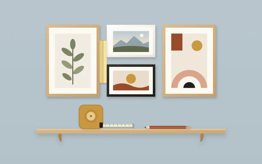 Four framed pictures on a dusty blue wall with even gaps, a folded paper strip held between two frames as a spacer